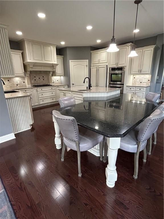 kitchen featuring a sink, a large island with sink, backsplash, dark wood-style floors, and recessed lighting