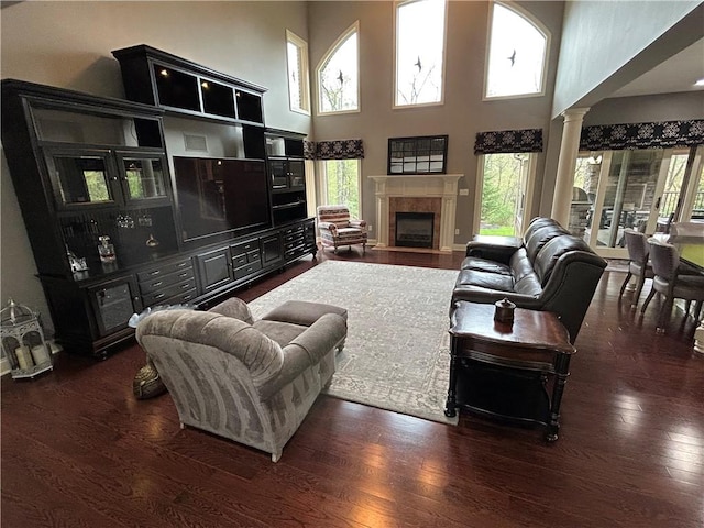 living room featuring wood finished floors, a high ceiling, ornate columns, and a tiled fireplace