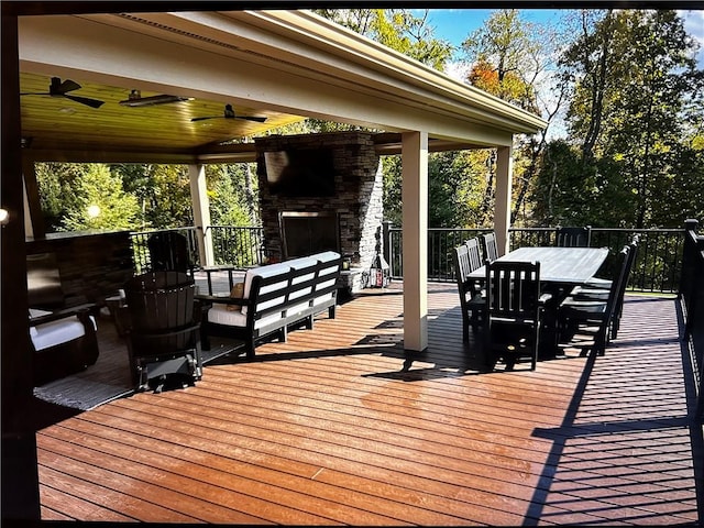 wooden terrace with an outdoor stone fireplace, outdoor dining area, and ceiling fan