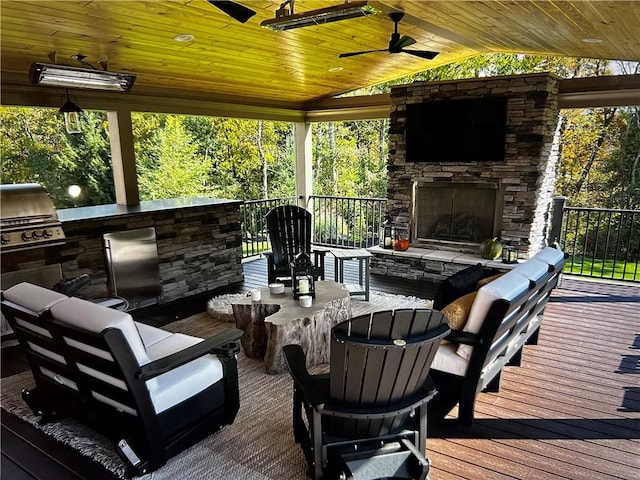 wooden terrace featuring an outdoor kitchen, an outdoor living space with a fireplace, and ceiling fan
