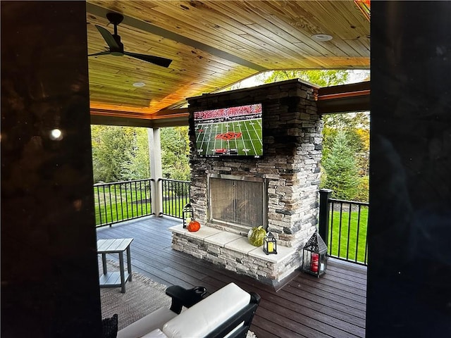 wooden terrace with an outdoor stone fireplace and ceiling fan