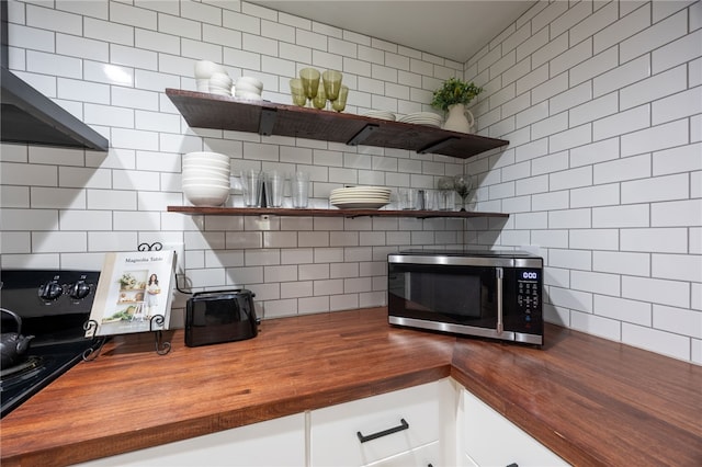 kitchen featuring wooden counters, stainless steel microwave, decorative backsplash, open shelves, and white cabinetry