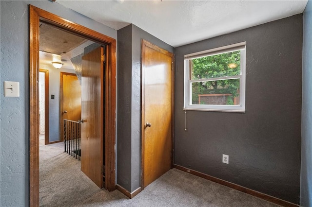 corridor with carpet, a textured wall, and baseboards