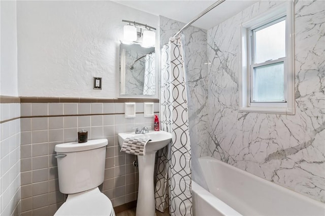 bathroom with tile walls, toilet, shower / bath combination with curtain, and a wainscoted wall