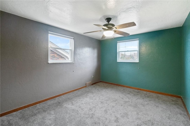 carpeted empty room with a textured wall, baseboards, and a ceiling fan