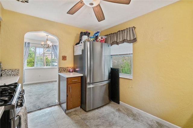 kitchen with appliances with stainless steel finishes, a chandelier, arched walkways, brown cabinets, and light countertops