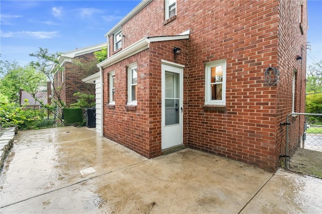 view of side of home featuring fence, brick siding, and a patio