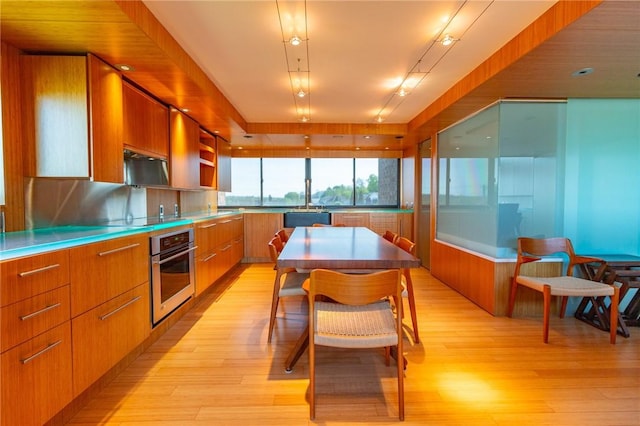 kitchen featuring stainless steel oven, brown cabinets, modern cabinets, and light wood-style flooring