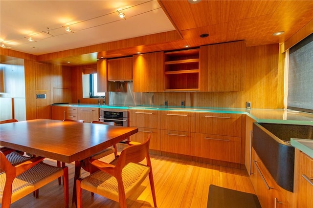 kitchen with stainless steel counters, modern cabinets, brown cabinetry, wood walls, and light wood-style floors