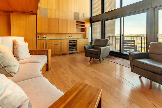 living room featuring a towering ceiling, beverage cooler, light wood-style floors, and bar