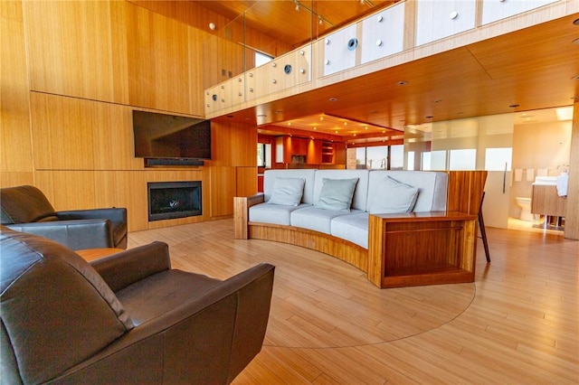 living area with a fireplace, wood finished floors, a towering ceiling, and wooden walls