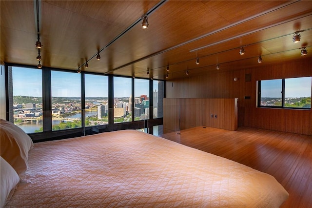 bedroom with track lighting, wood finished floors, a city view, wood walls, and a water view