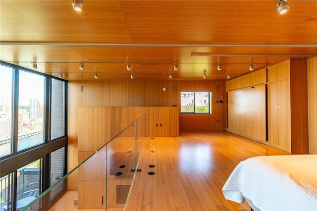 bedroom with track lighting, wooden walls, light wood-style floors, and wood ceiling