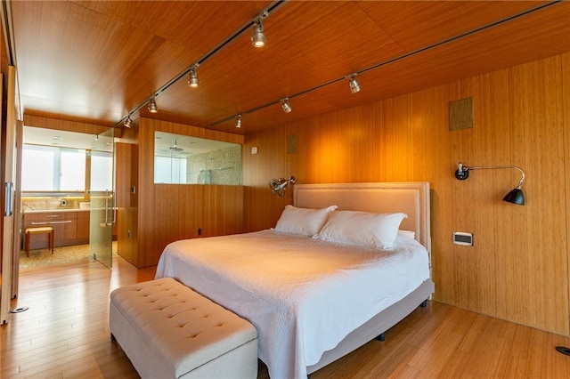 bedroom featuring rail lighting, wood walls, and light wood-style floors
