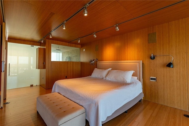 bedroom with rail lighting, wooden walls, and wood finished floors
