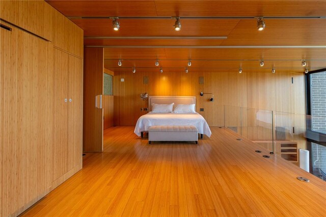 bedroom featuring rail lighting, wood finished floors, and wood walls