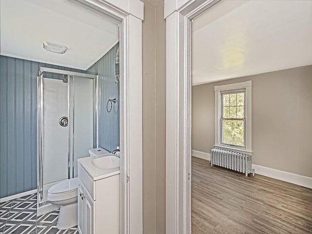 bathroom with radiator heating unit, a stall shower, baseboards, toilet, and vanity