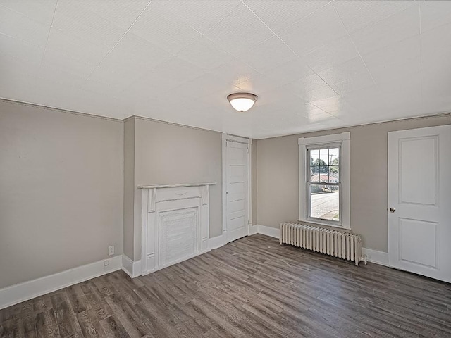 unfurnished living room featuring radiator heating unit, wood finished floors, and baseboards