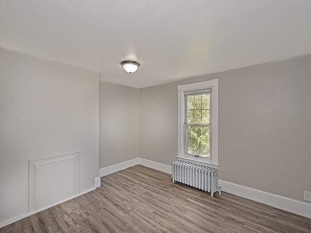 unfurnished room with radiator, wood finished floors, and baseboards