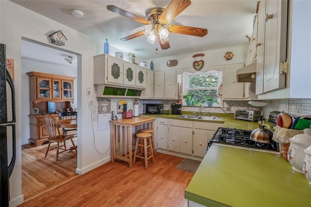 kitchen with a sink, black appliances, light wood-style floors, backsplash, and a ceiling fan