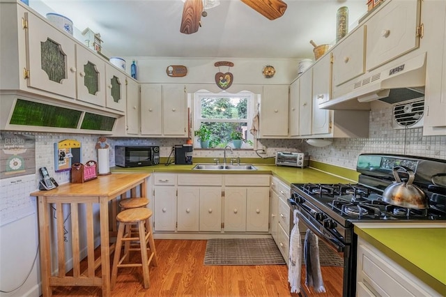 kitchen with black appliances, a sink, under cabinet range hood, light wood-style floors, and tasteful backsplash