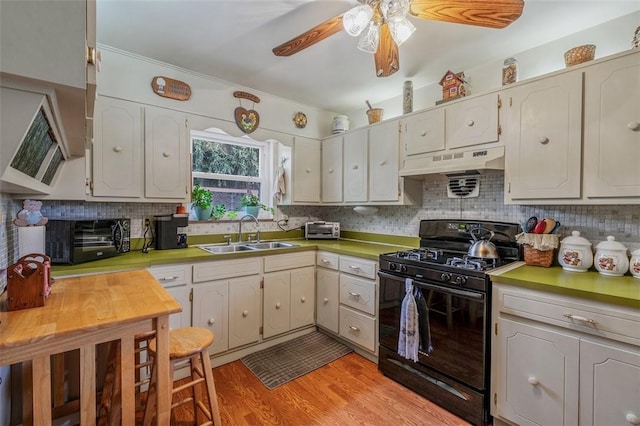 kitchen with black gas stove, a sink, under cabinet range hood, and decorative backsplash
