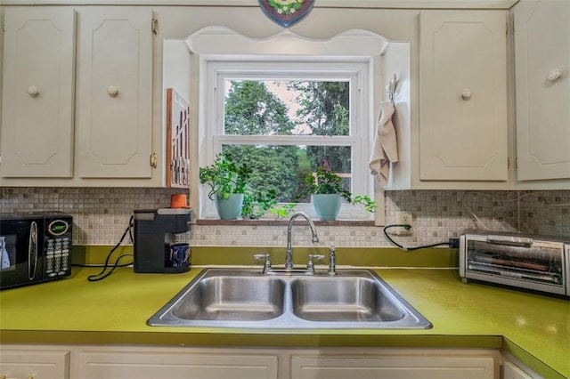 kitchen with a sink, black microwave, tasteful backsplash, light countertops, and white cabinets