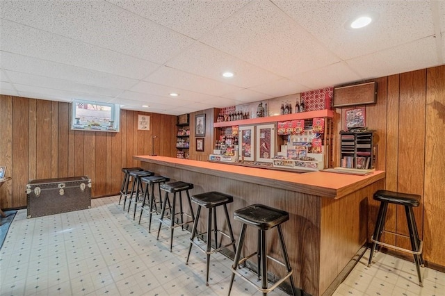indoor dry bar featuring light floors, a drop ceiling, and wooden walls