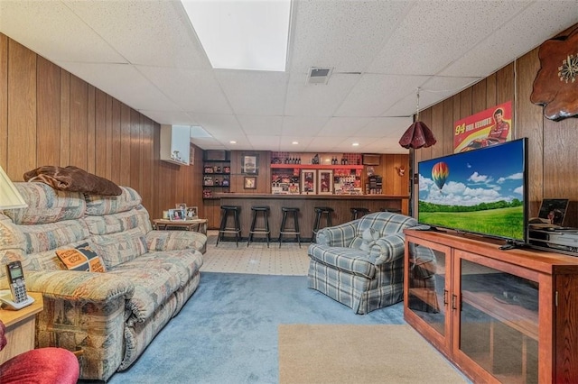 carpeted living room featuring wooden walls, a dry bar, and a drop ceiling