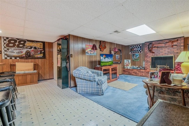 living room featuring a drop ceiling, tile patterned floors, wooden walls, and a fireplace