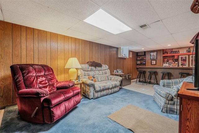carpeted living area featuring a bar, wood walls, and a paneled ceiling