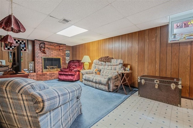 living area with tile patterned floors, a drop ceiling, a fireplace, and wooden walls