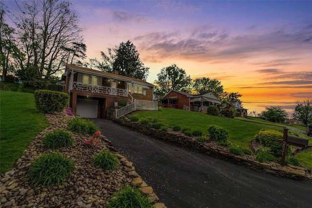 view of front of house featuring driveway, a lawn, an attached garage, a porch, and stairs