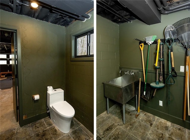 bathroom with toilet, concrete block wall, and stone finish flooring