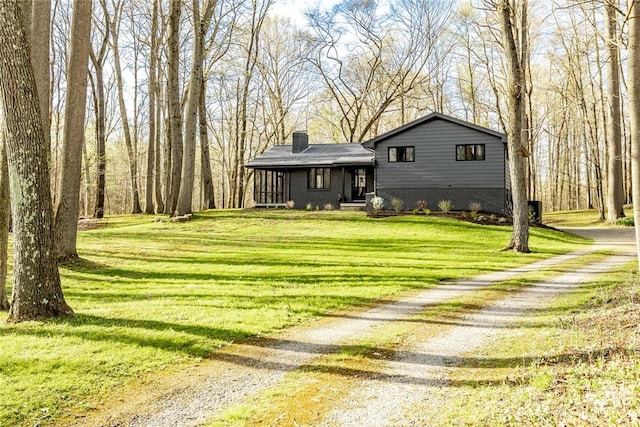 view of front of home featuring driveway, a chimney, and a front yard