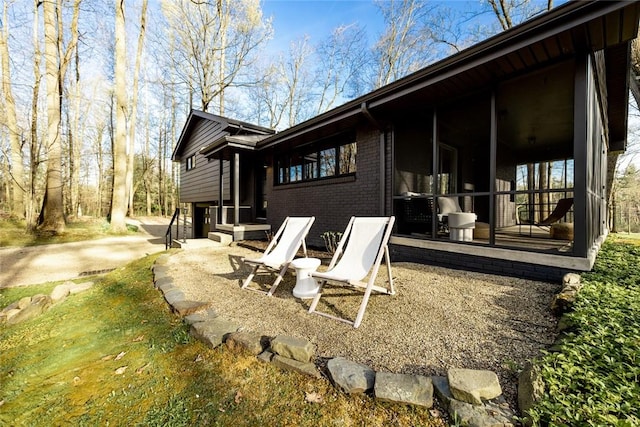 view of side of property with a sunroom, brick siding, and a patio area