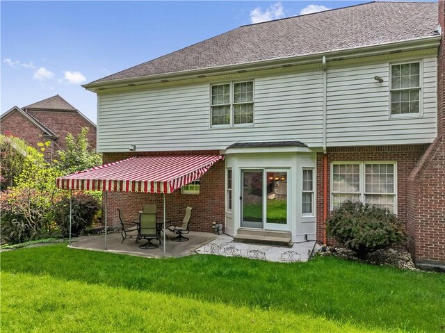 back of house with a patio area, a lawn, and brick siding