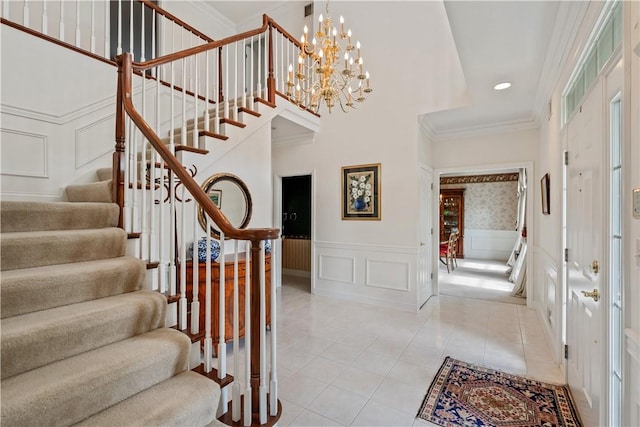 foyer with a decorative wall, stairs, a chandelier, light tile patterned floors, and ornamental molding