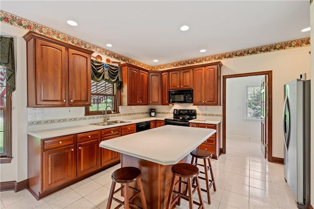kitchen featuring black appliances, a sink, a breakfast bar, light countertops, and healthy amount of natural light