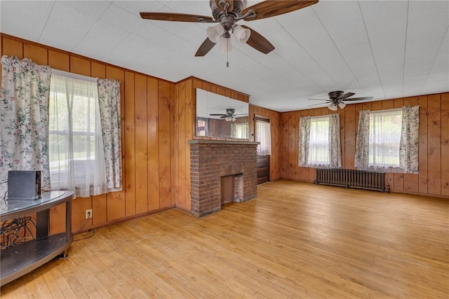 living area with radiator, hardwood / wood-style flooring, a ceiling fan, a brick fireplace, and wooden walls