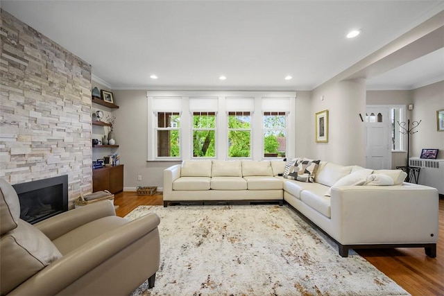living area featuring crown molding, wood finished floors, a stone fireplace, recessed lighting, and baseboards