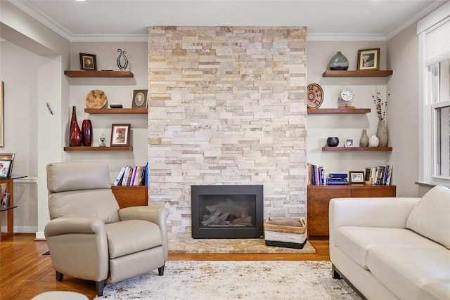living room with wood finished floors, crown molding, and a stone fireplace