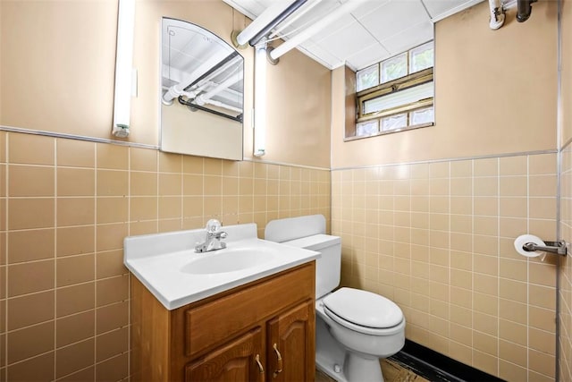 bathroom featuring toilet, tile walls, vanity, and a wainscoted wall