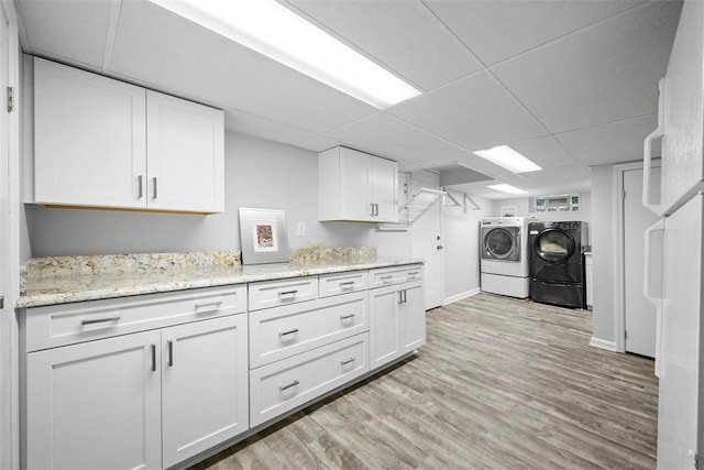 kitchen with washer and clothes dryer, white cabinetry, light wood-style floors, a paneled ceiling, and light stone countertops