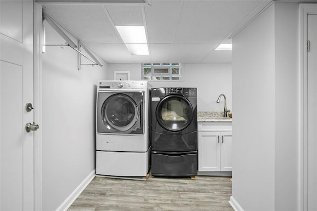 clothes washing area featuring washer and dryer, light wood finished floors, cabinet space, and baseboards