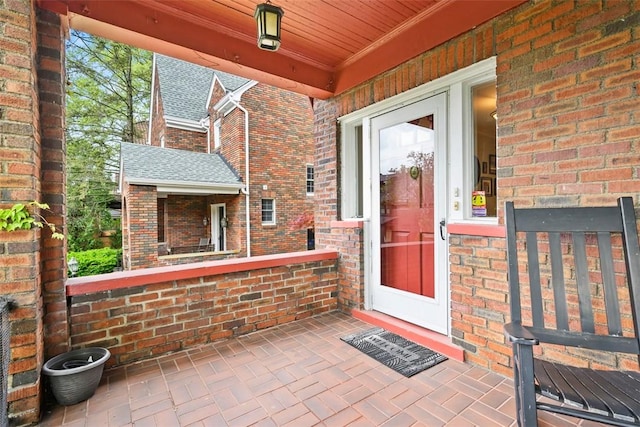 view of exterior entry with a porch and brick siding