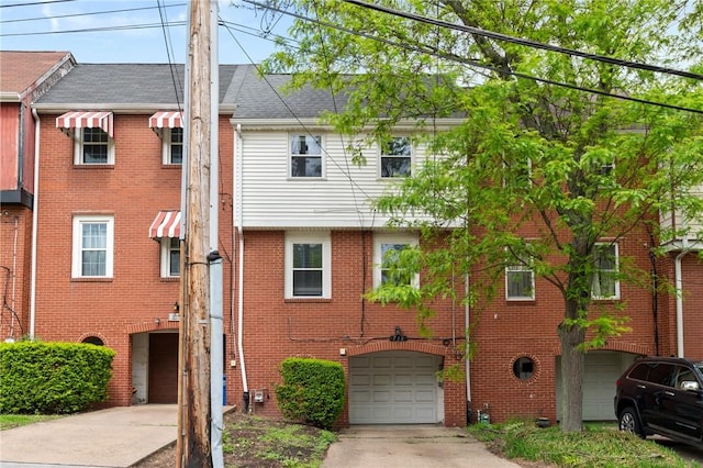 townhome / multi-family property featuring an attached garage, driveway, brick siding, and roof with shingles