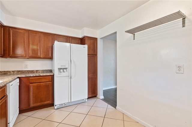 kitchen with white appliances, brown cabinetry, light tile patterned floors, and baseboards