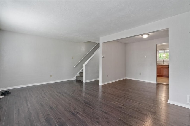 unfurnished living room featuring dark wood-style flooring, stairs, baseboards, and a sink