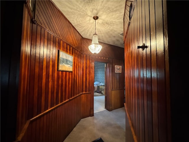 corridor with wood walls, a chandelier, carpet floors, and a textured ceiling